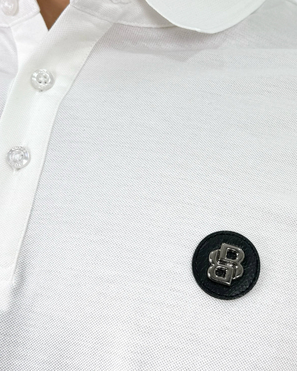 Camisa tipo polo blanca para hombre, cuello y botones, con logo metálico en pecho, tela premium y corte moderno