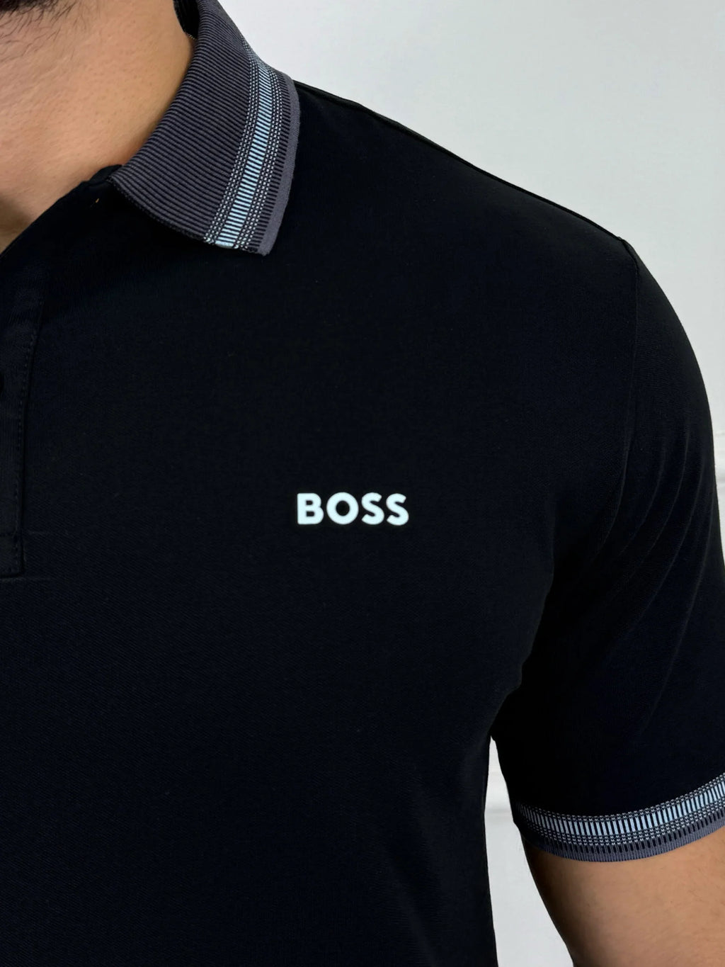 Camisa polo negra para hombre con logo BOSS, cuello y puños con detalles en azul claro, estilo moderno y premium.
