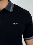 Camisa polo negra para hombre con logo BOSS, cuello y puños con detalles en azul claro, estilo moderno y premium.